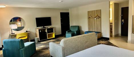 A hotel room with a bed, a desk with a chair, a television, a mirror, and a sofa.