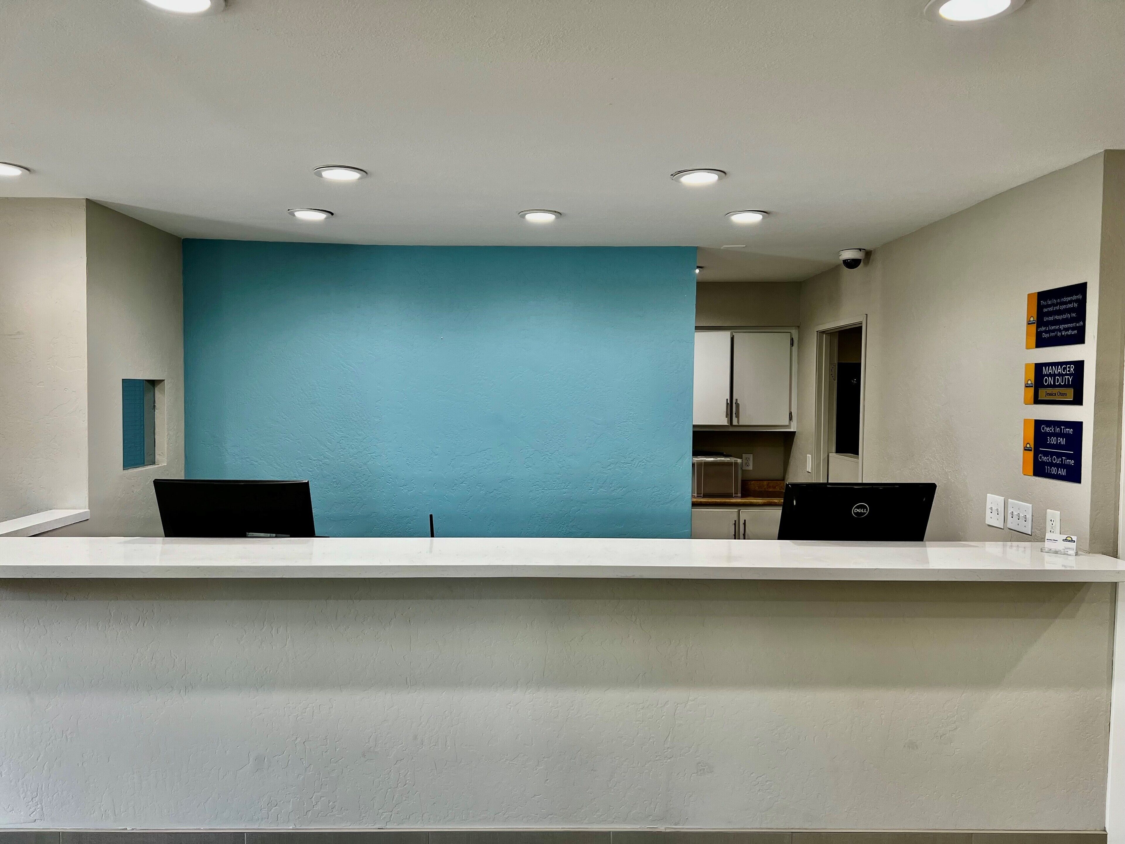 A reception desk with two black chairs, a blue accent wall, and a kitchen area in the background.