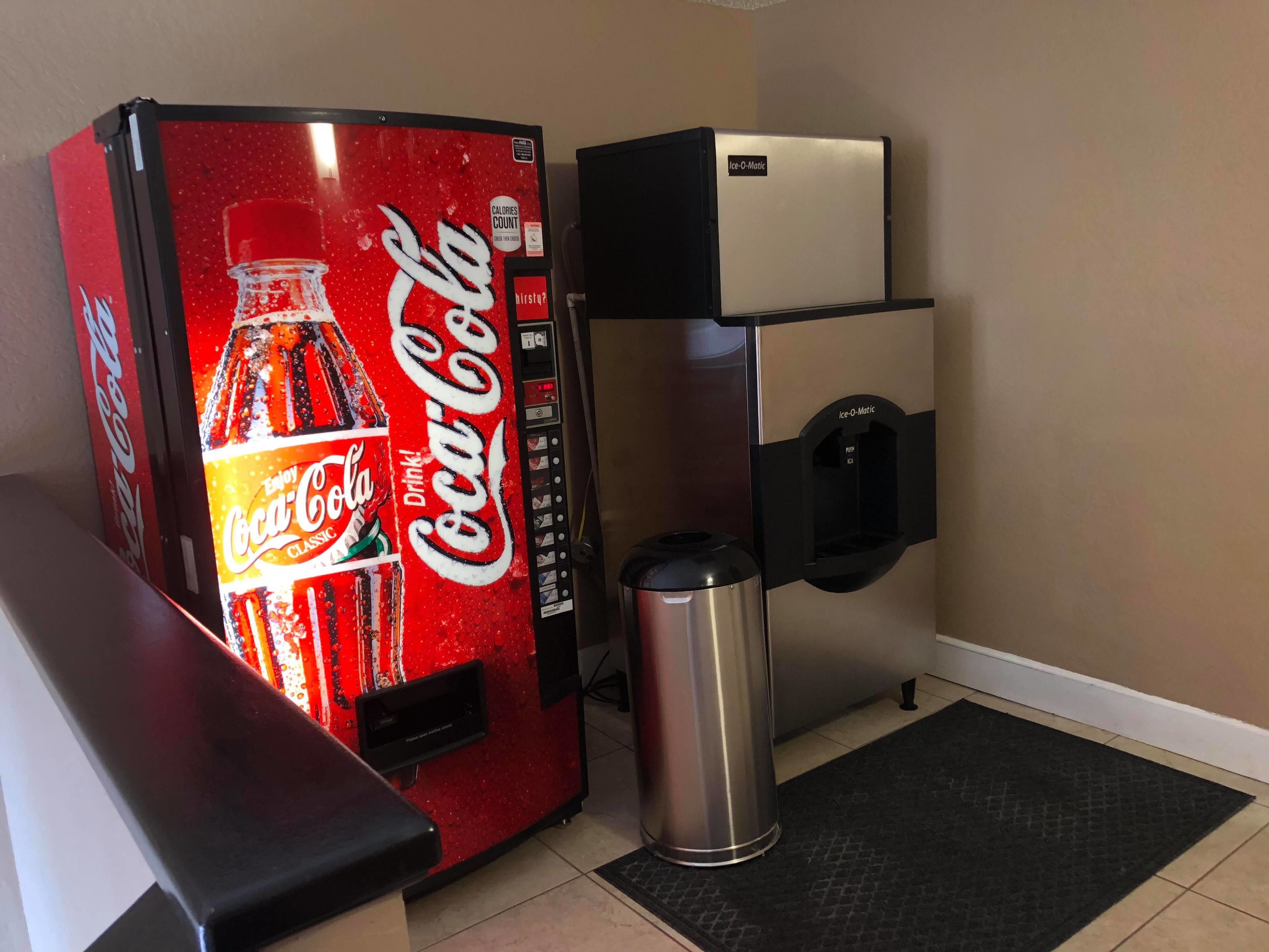 A Coca-Cola vending machine and an Ice-O-Matic dispenser in a room with a tiled floor and a black doormat.