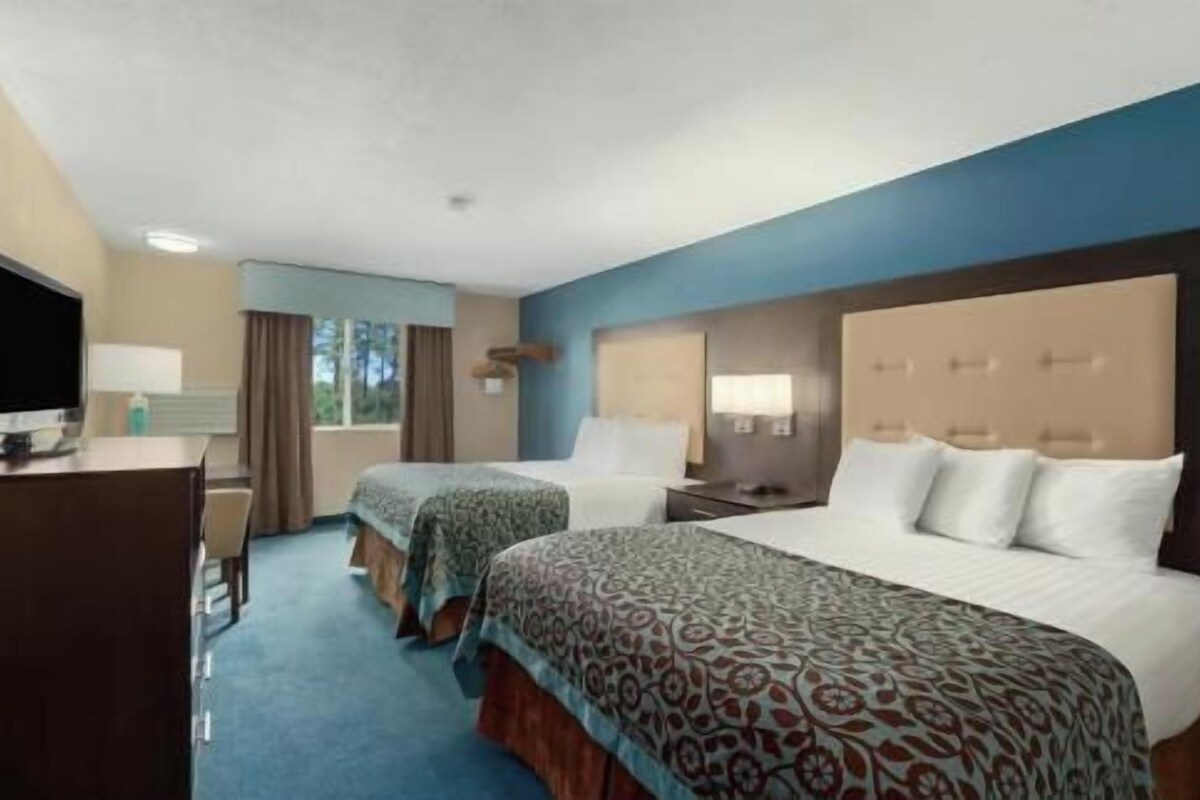 A hotel room with two beds, a desk with a chair, a television, and a window with curtains.