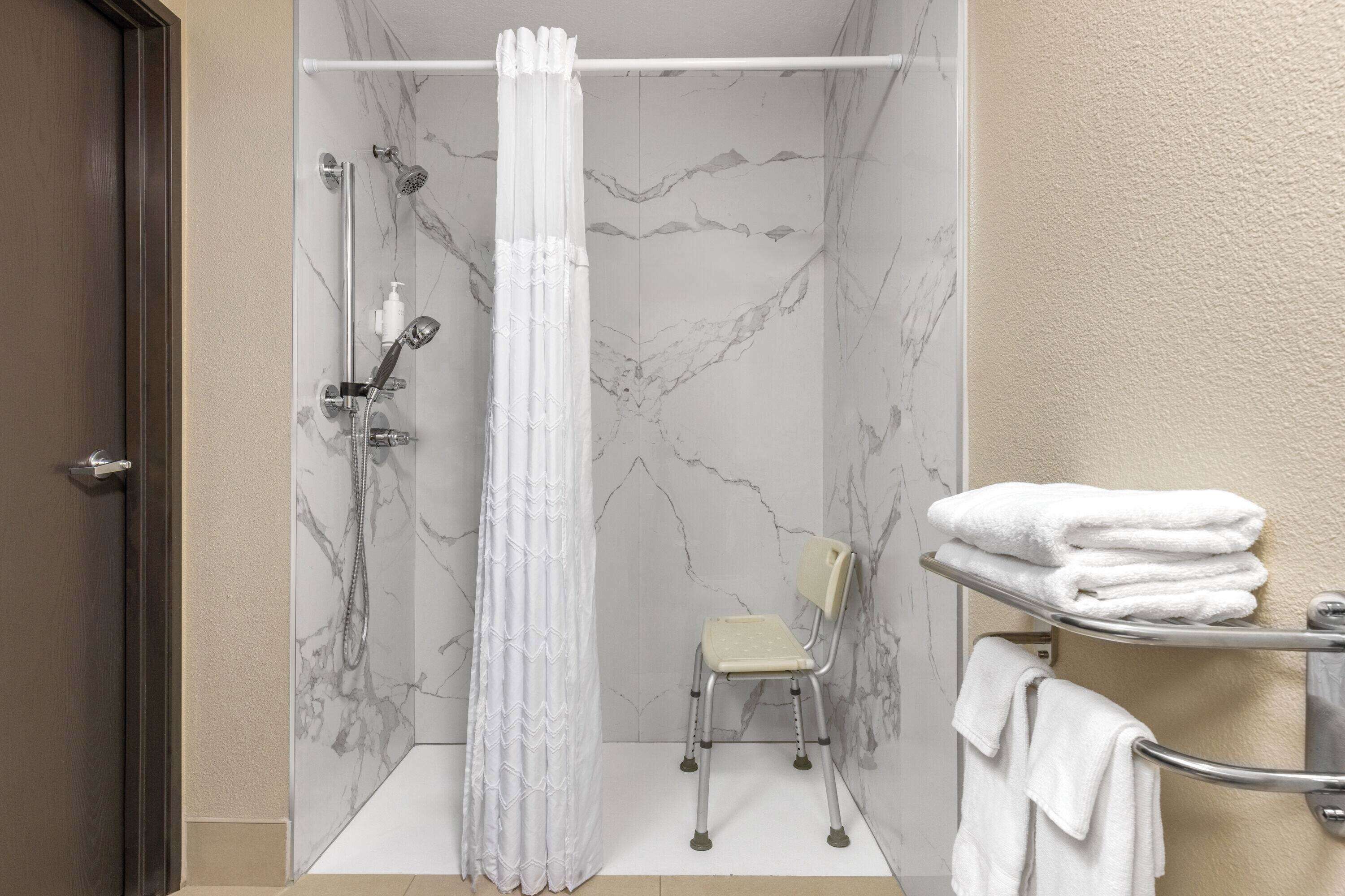 A bathroom with a shower, a chair, and a towel rack.