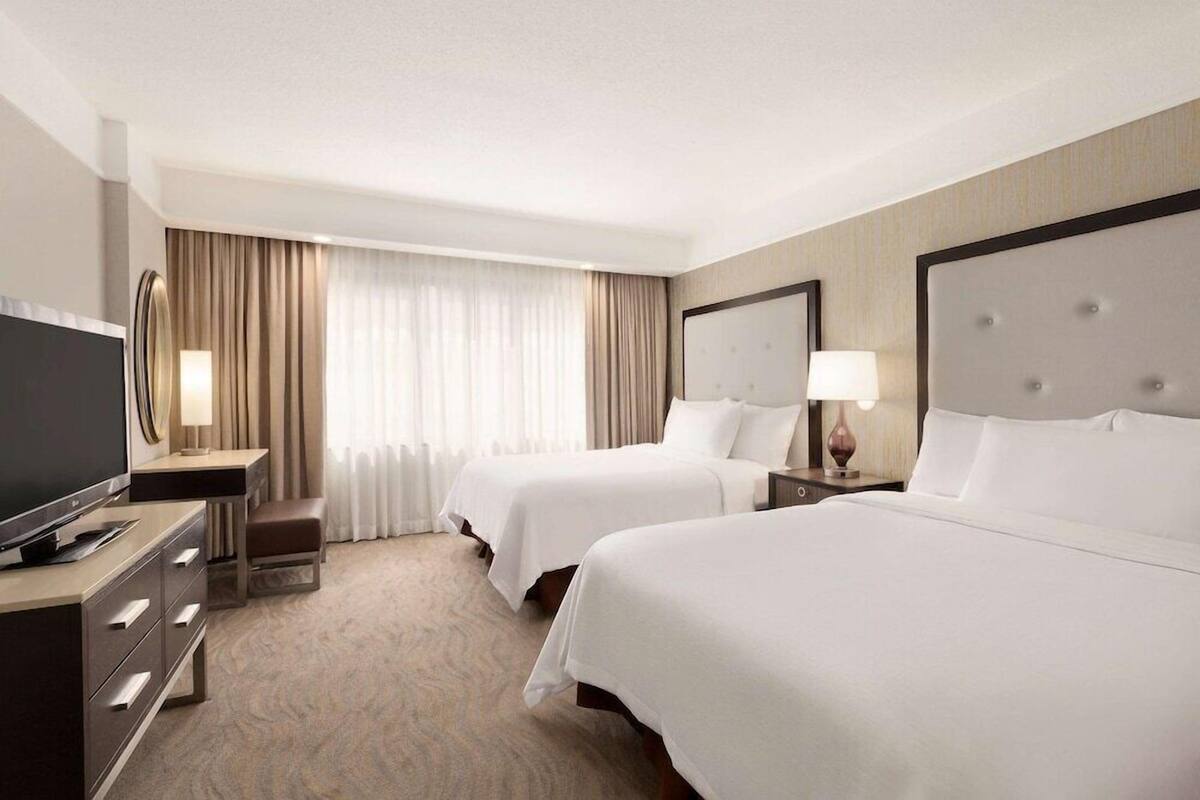 A hotel room with two beds, a TV, a desk with drawers, a lamp, and a large mirror.