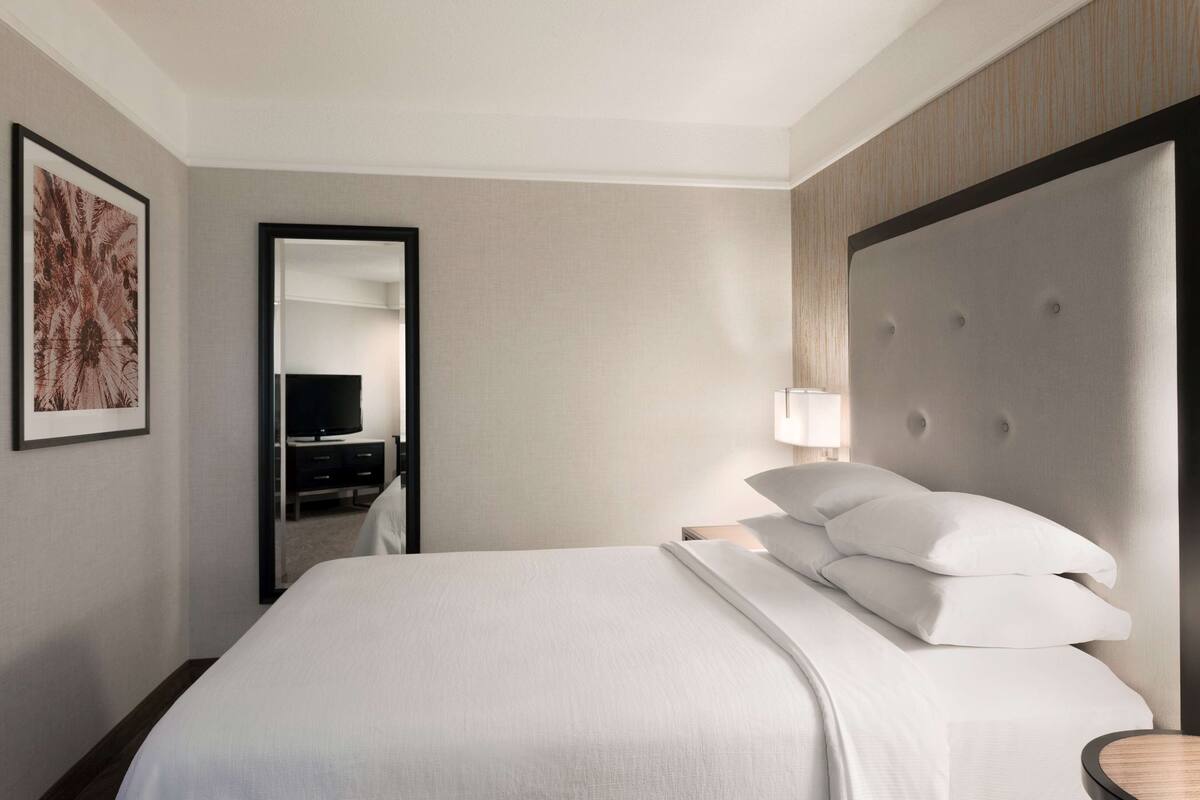 Ein Hotelzimmer mit einem großen Bett, einem Nachttisch, einem Spiegel und einem gerahmten Bild an der Wand.