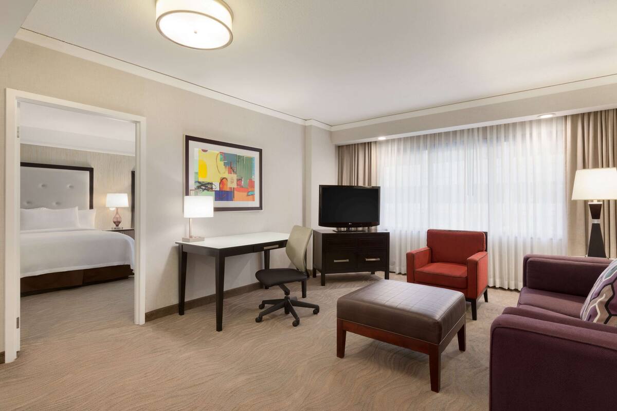 Ein Hotelzimmer mit Bett, Schreibtisch, Bürostuhl, Fernseher, rotem Sessel und einer Couch.