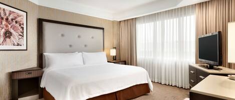 A hotel room with a large bed, a desk, a television, and a window with curtains.