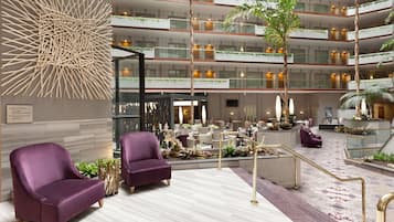 A modern hotel lobby with multiple floors, a reception area, and purple armchairs.