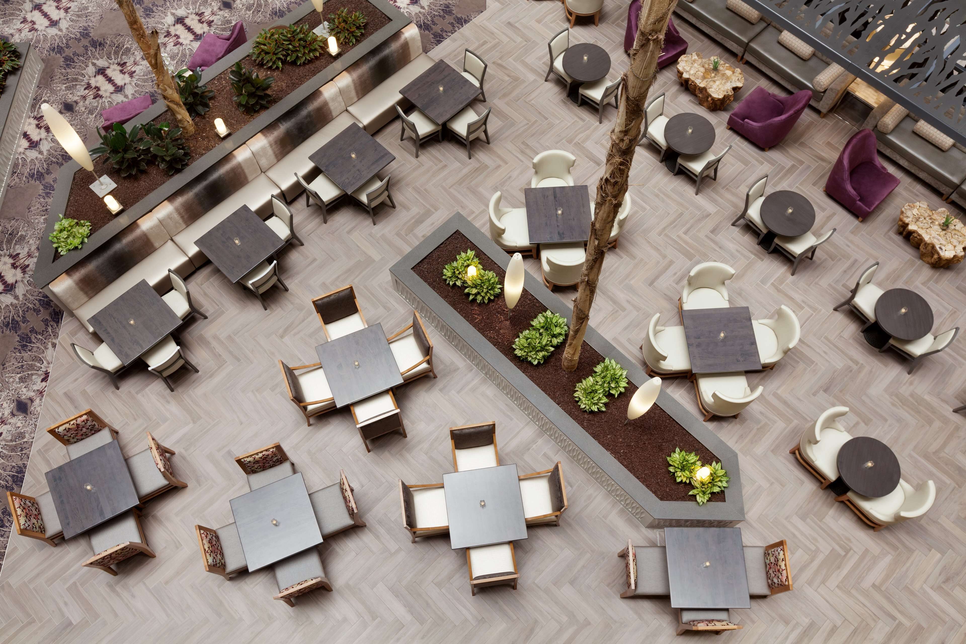 An outdoor seating area with multiple tables and chairs, surrounded by planters and a herringbone floor pattern.