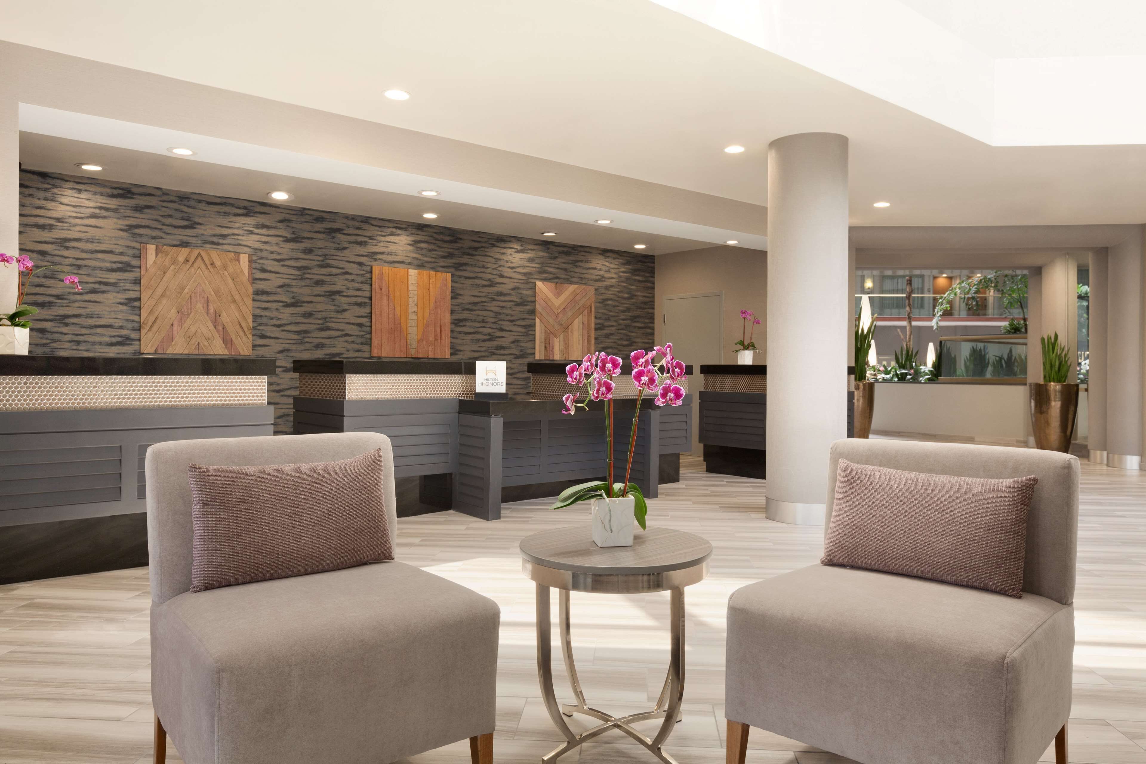 A modern reception area with a reception desk, two armchairs, a small round table, and decorative plants.