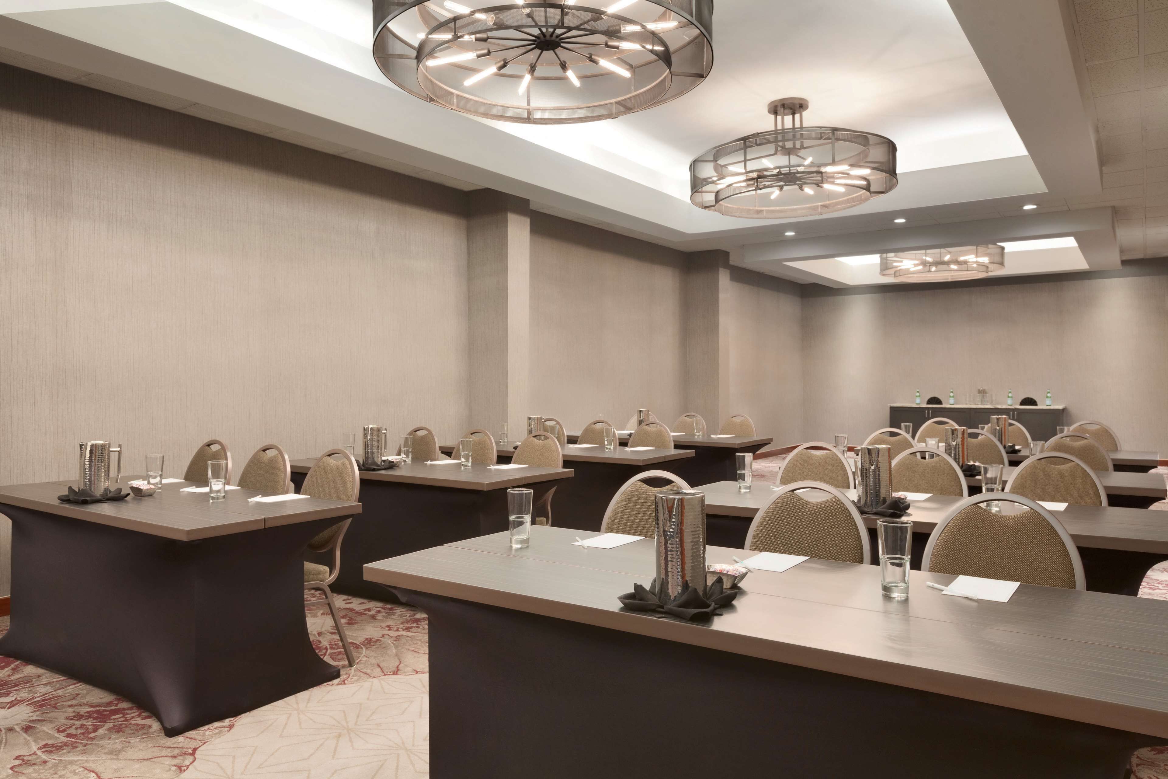 A conference room with multiple tables, chairs, and modern chandeliers.