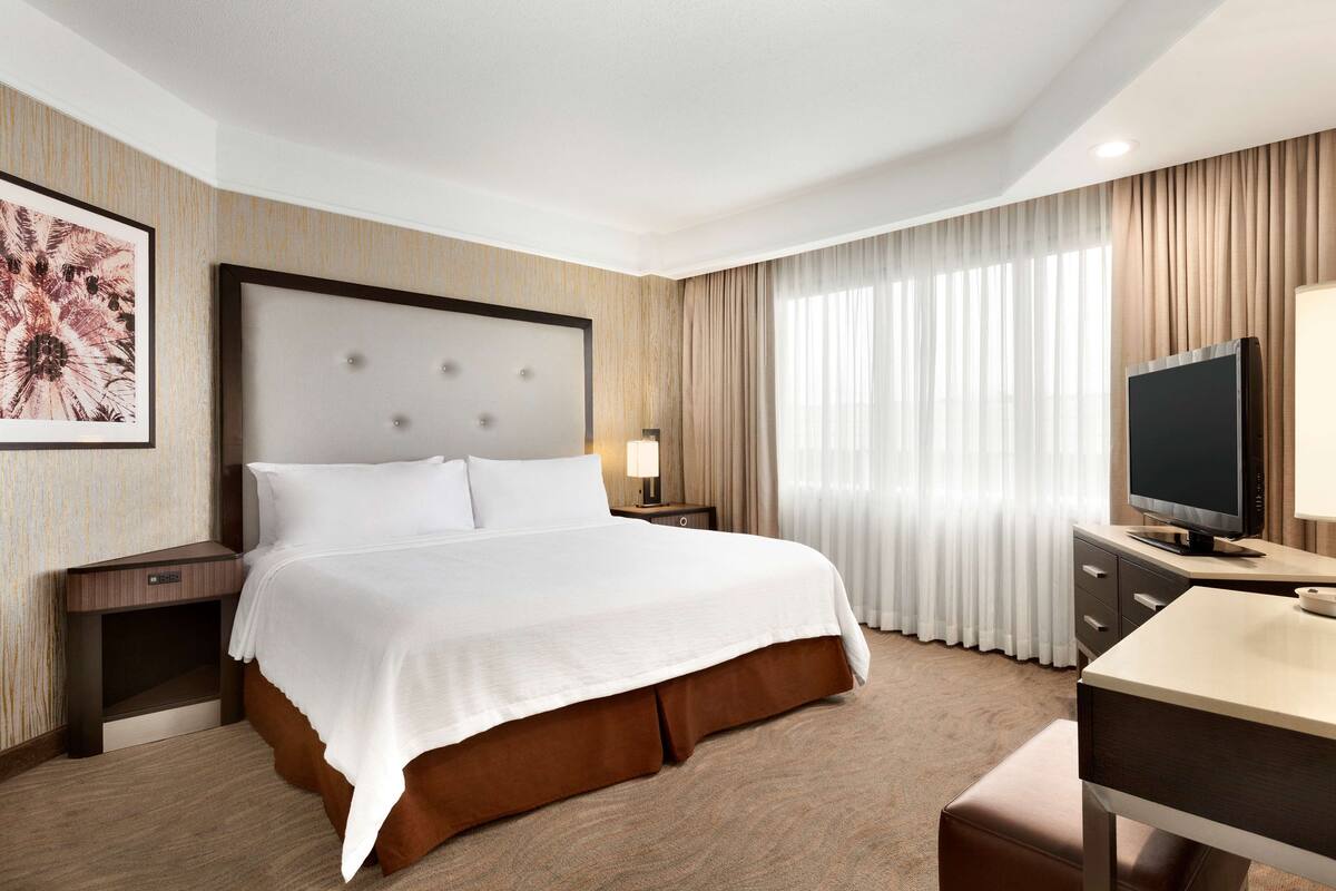 A hotel room with a large bed, a desk, a television, and a window with curtains.