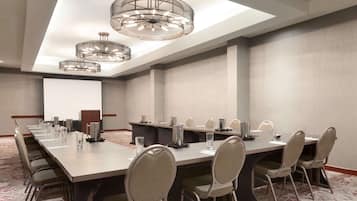A conference room with a long table, chairs, and a projector screen.