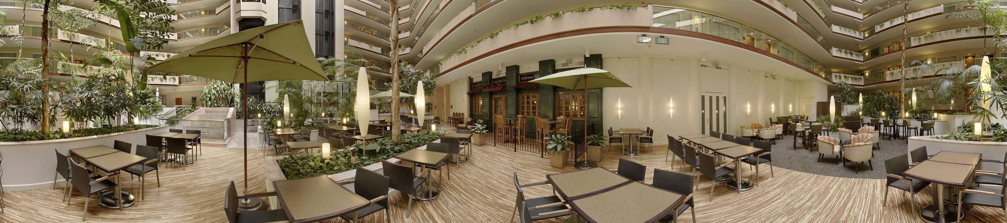 A spacious indoor atrium with multiple dining areas, surrounded by lush greenery and modern architecture.
