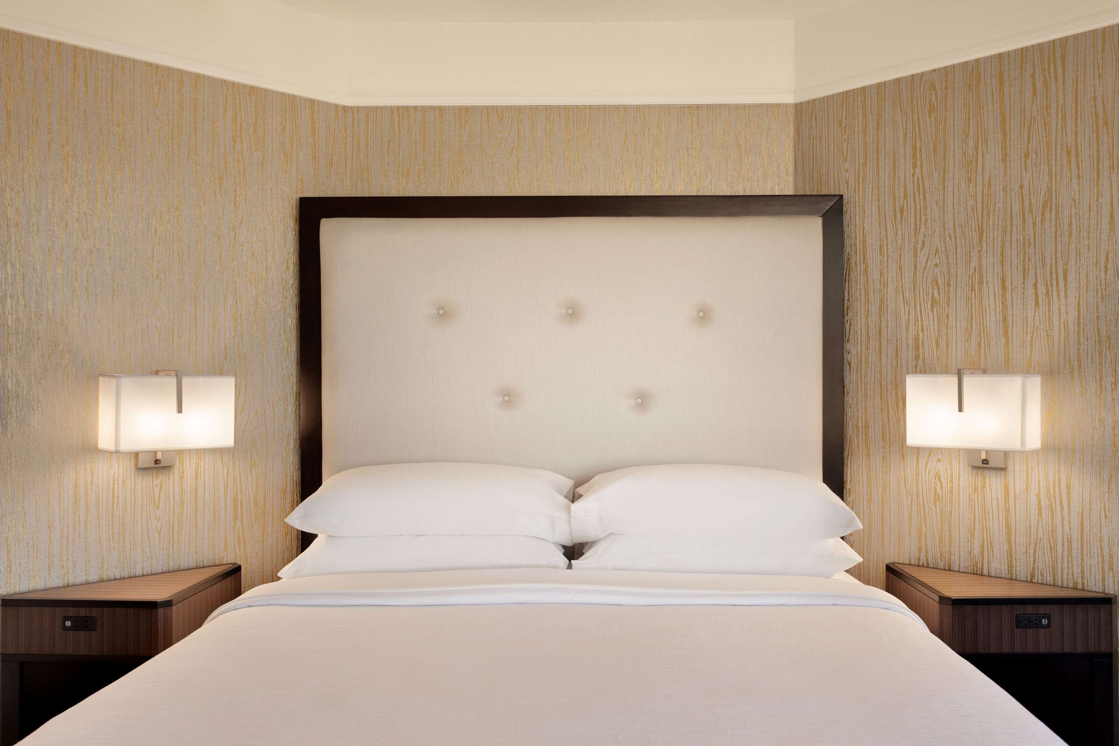A hotel room with a large bed, two bedside tables, and wall-mounted lamps.