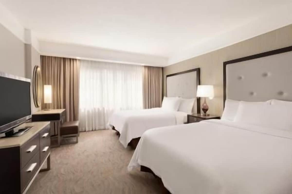 Une chambre d’hôtel avec deux lits, un bureau, une télévision et une fenêtre avec des rideaux.