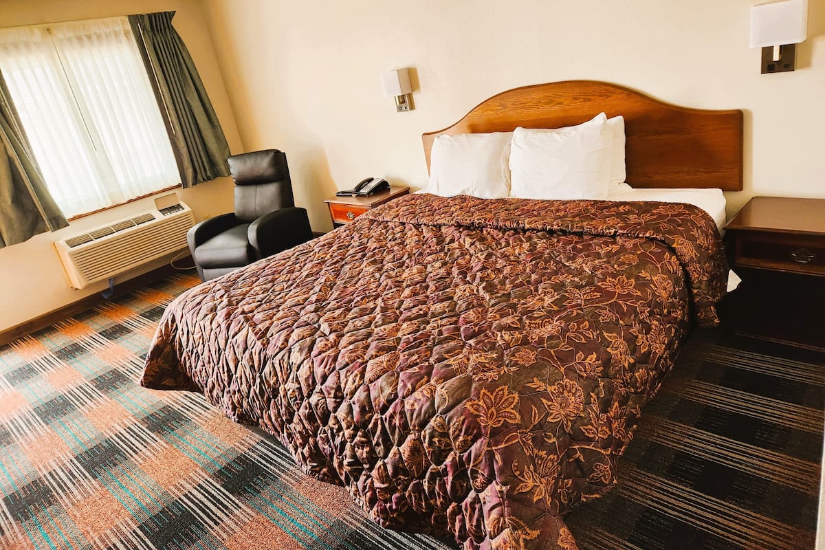 A hotel room with a large bed, a chair, a desk, and a window with curtains.