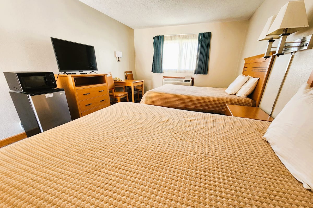 A hotel room with two beds, a desk, a television, a refrigerator, and a window with curtains.
