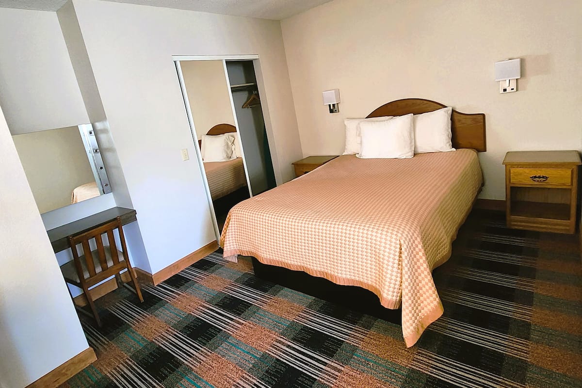 A bedroom with a bed, bedside tables, a desk, a chair, a wardrobe, and a mirror.