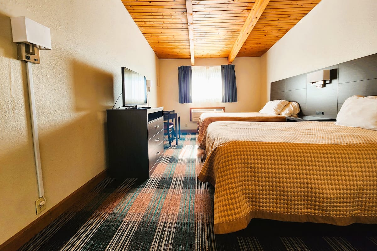 A hotel room with two beds, a desk, a chair, a TV, and a window with curtains.