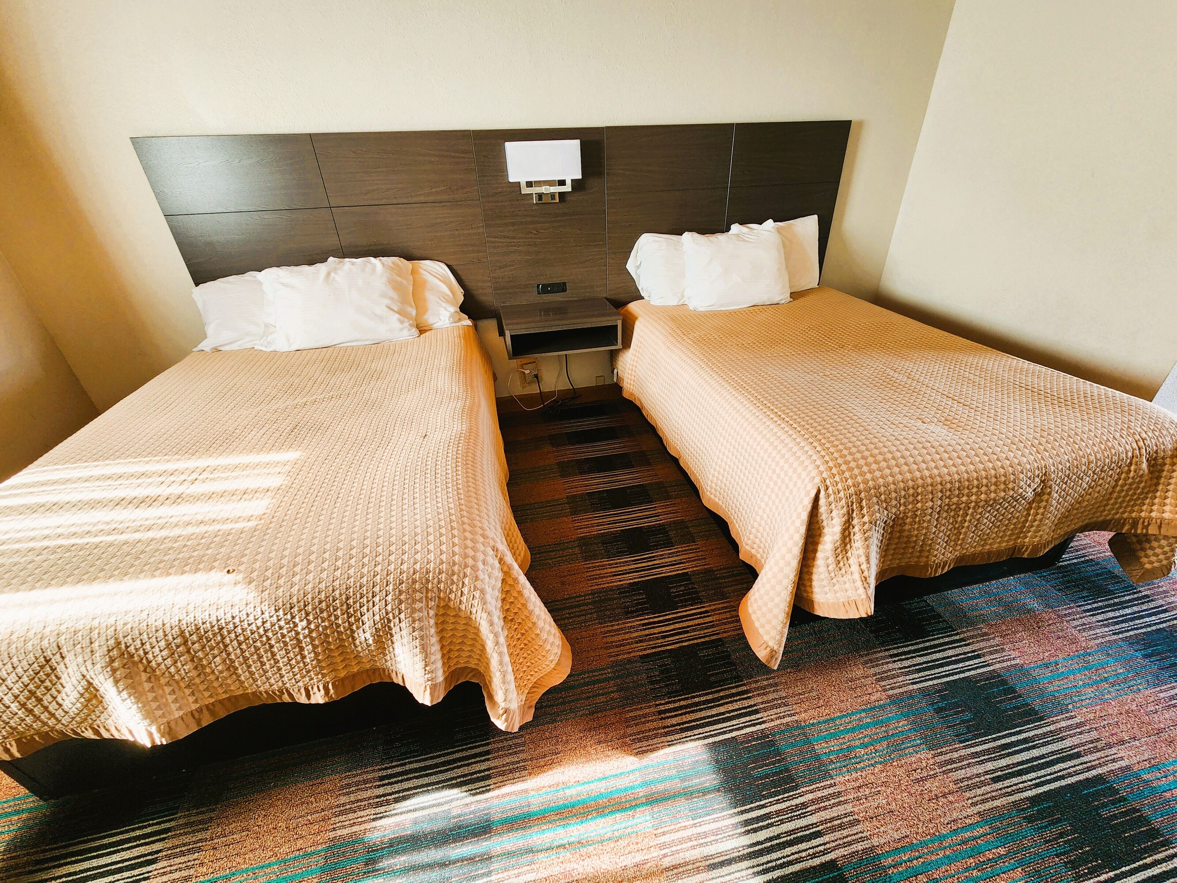 A hotel room with two single beds, a dark headboard, a small bedside table, and a patterned carpet.