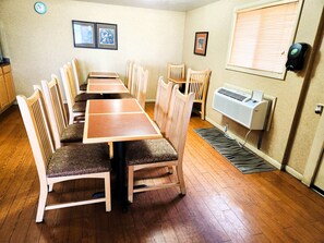 A dining area with a long wooden table and matching chairs, a clock, framed pictures on the wall, and a window with blinds. - Americas Best Inn Iola (Iola)
