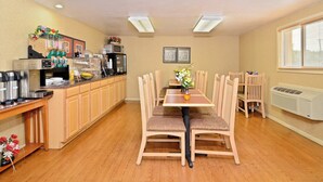 Uma área de refeições com mesa e cadeiras de madeira, um espaço para café e quadros nas paredes.