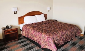 A hotel room with a wooden bed, a nightstand with a phone, and two wall-mounted lamps. - Countryside Inn Iola (Iola)