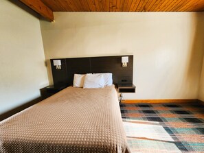 A hotel room with a bed, nightstands, wall-mounted lamps, and a patterned carpet. - Americas Best Inn Iola (Iola)
