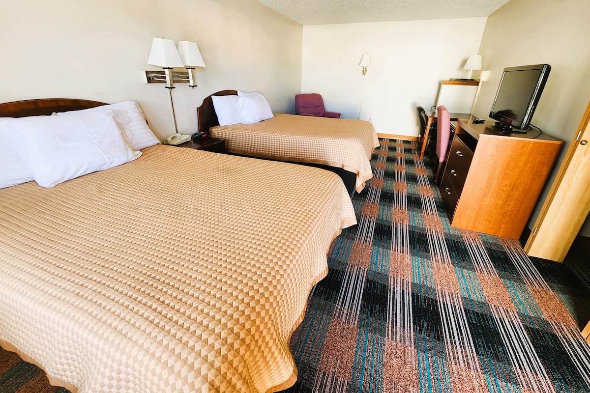 A hotel room with two beds, a desk, a chair, a TV, and a wardrobe.