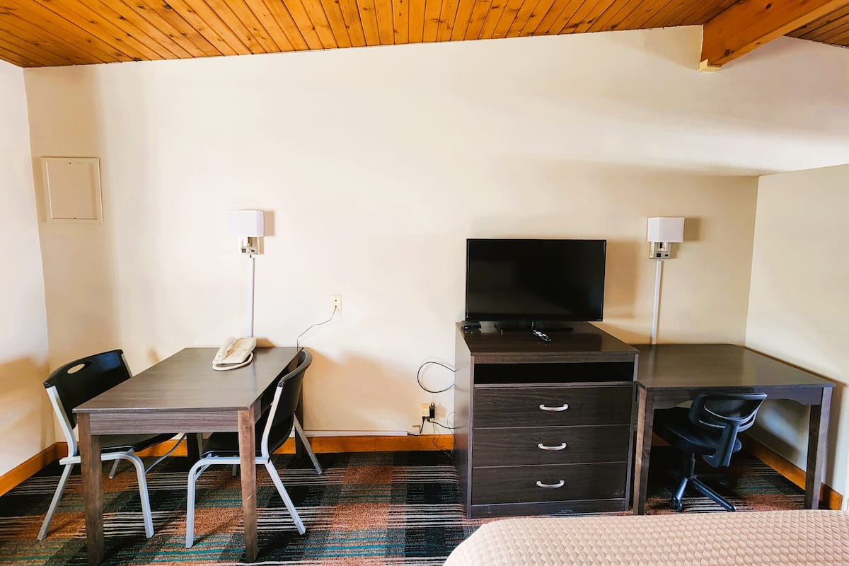 A hotel room with a wooden ceiling, a desk with a computer, a TV, a chair, and a bed.