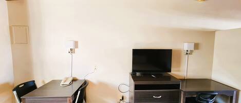 Habitación de hotel con techo de madera, un escritorio con computadora, televisor, una silla y una cama.