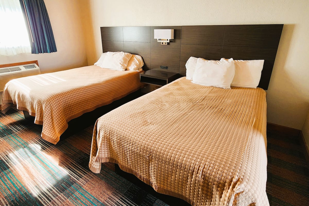 A hotel room with two beds, a headboard, a nightstand, and a window with curtains.