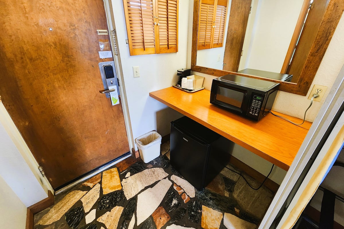 A bathroom with a wooden door, a mirror, a microwave, and a trash bin.