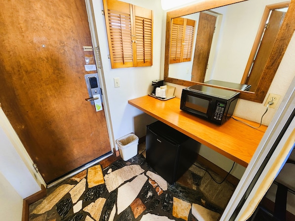 A bathroom with a wooden door, a mirror, a microwave, and a trash bin. - Countryside Inn Iola (Iola)