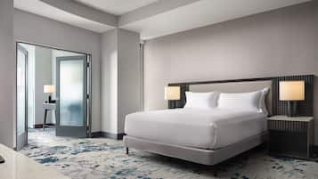 A modern hotel room with a large bed, two bedside lamps, a nightstand, a desk, and a patterned carpet.