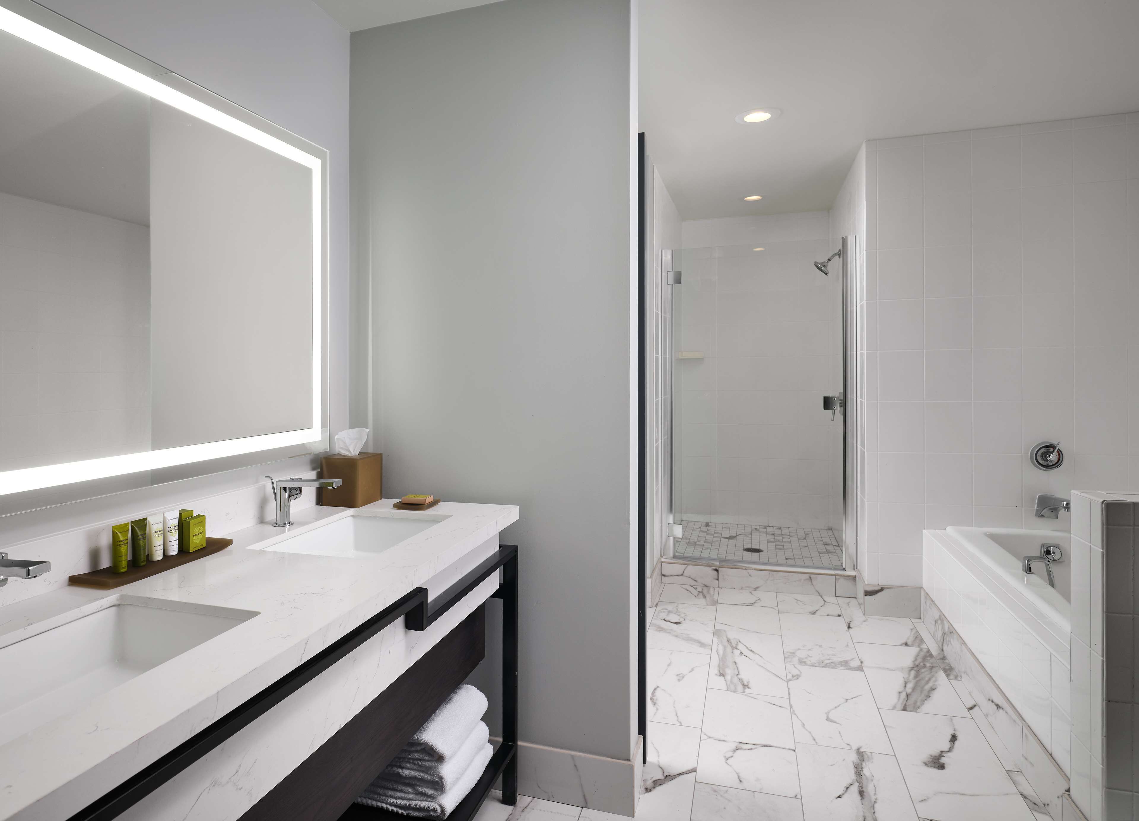 A modern bathroom with a large mirror, white marble countertops, a glass-enclosed shower, and a separate bathtub.