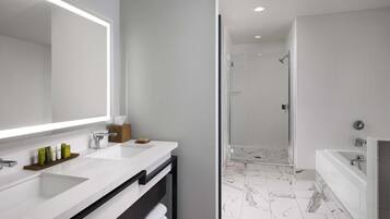 A modern bathroom with a large mirror, white marble countertops, a glass-enclosed shower, and a separate bathtub.