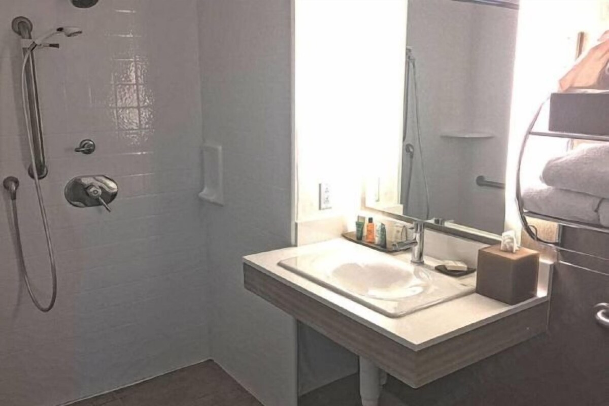 A bathroom with a shower, a sink, a mirror, and a towel rack.