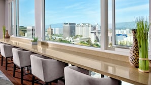 Una habitación de hotel moderna con una larga encimera, varias sillas y amplias ventanas con vistas a la ciudad.