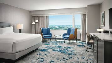 A hotel room with a large bed, two armchairs, a desk, and a view of the city.