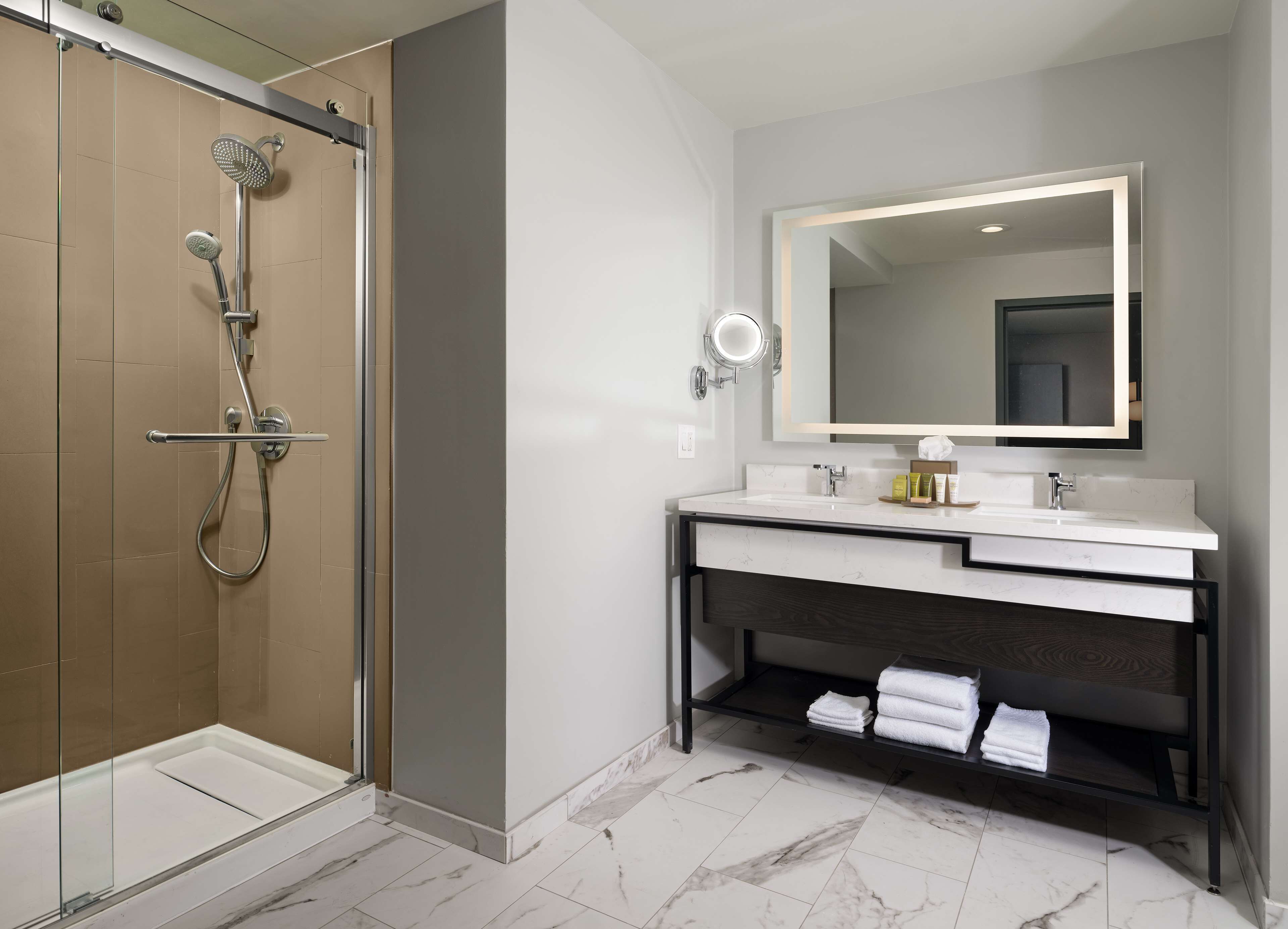 A modern bathroom with a glass-enclosed shower, a large mirror, and a vanity with a marble countertop.