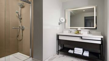A modern bathroom with a glass-enclosed shower, a large mirror, and a vanity with a marble countertop.
