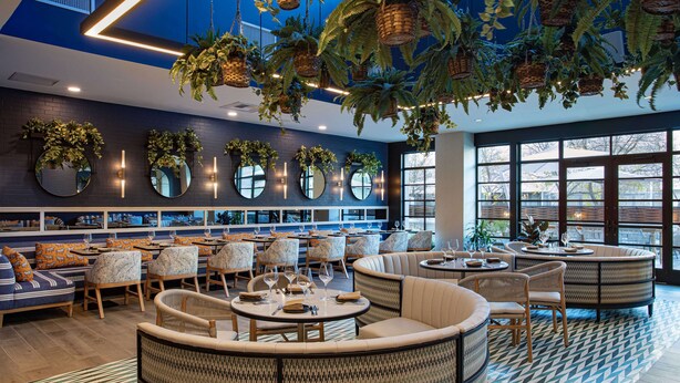 Un restaurante moderno con mesas redondas, asientos acolchados y plantas colgantes.