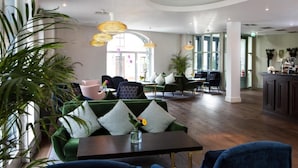 A modern hotel lobby with a green sofa, dining area, and large windows.