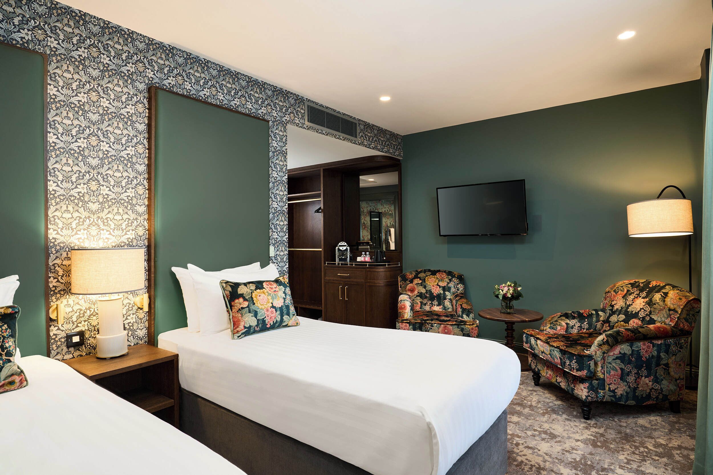 Habitación de hotel con dos camas, televisión, lámpara, silla y una mesita.