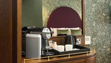 Habitación de hotel con estación de café, que incluye una cafetera, jarra de vidrio y bandeja con tazas y un termo.