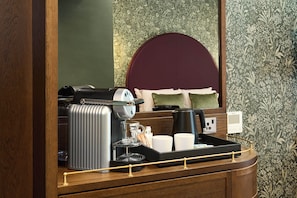 A hotel room with a coffee station, including a coffee maker, a glass carafe, and a tray with cups and a thermos.