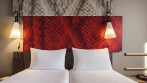 A double bed with white linens, two bedside lamps, and a red textured wall above. - Hôtel ibis Cambrai (Fontaine-Notre-Dame)