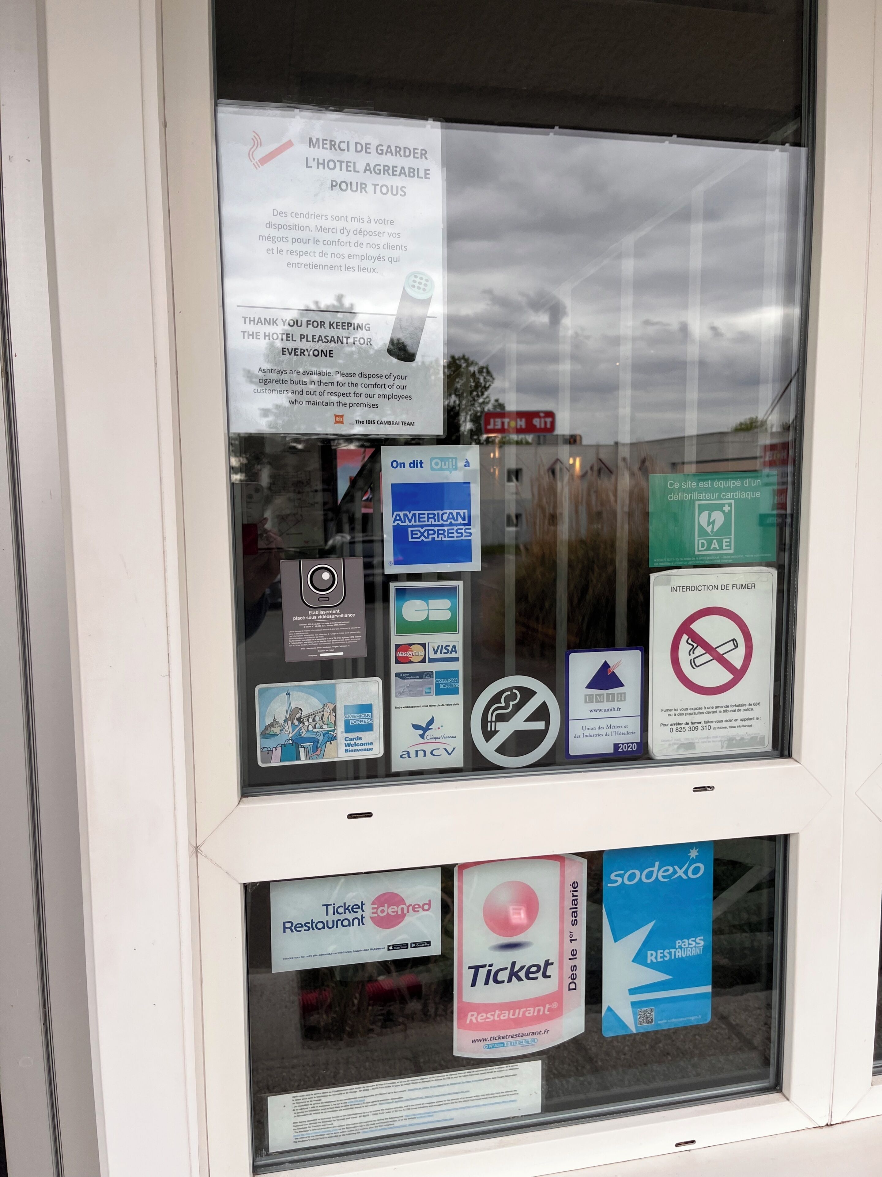 Una ventana con varios carteles, incluyendo una nota de agradecimiento por mantener agradable el hotel, un letrero de no fumar y múltiples logotipos de métodos de pago.