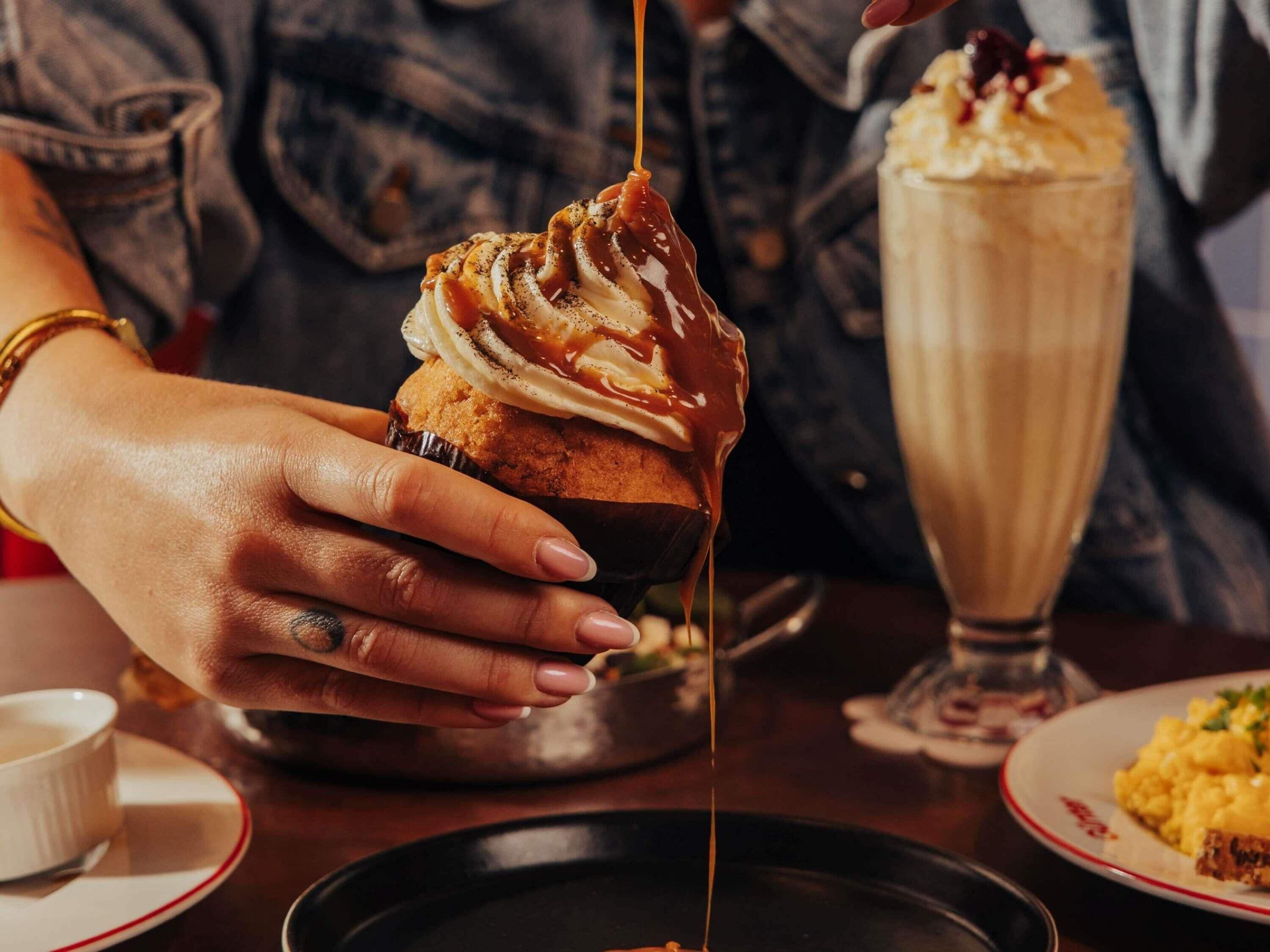 A hand holding a dessert with caramel sauce being poured over it.