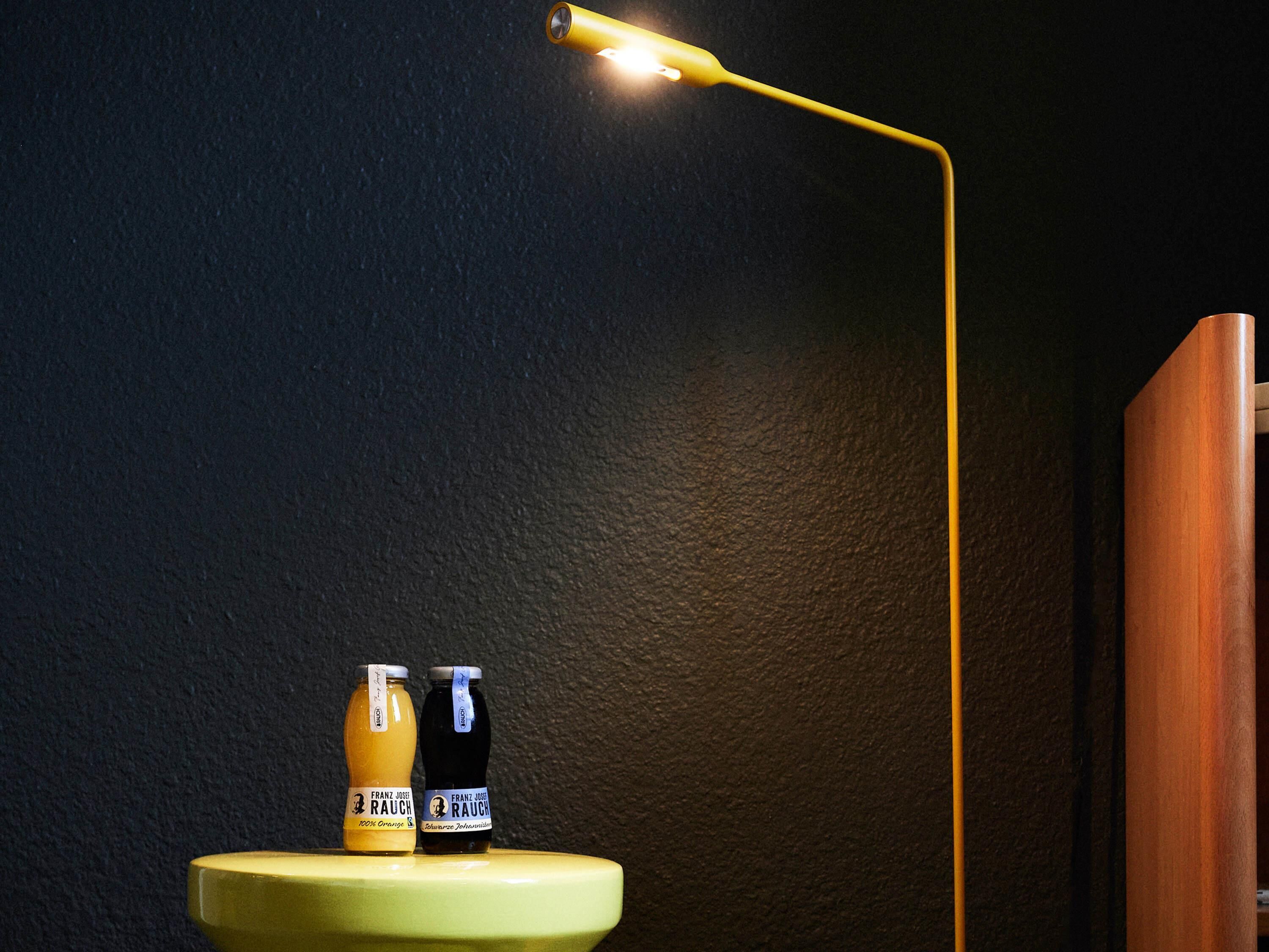 A yellow desk lamp illuminating two bottles on a green surface against a dark wall.